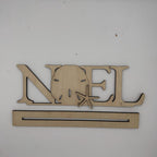 A wooden personalized name sign spelling 'NOEL' with a sand dollar and starfish cutout, mounted on a plain white wall above a long rectangular wooden base.