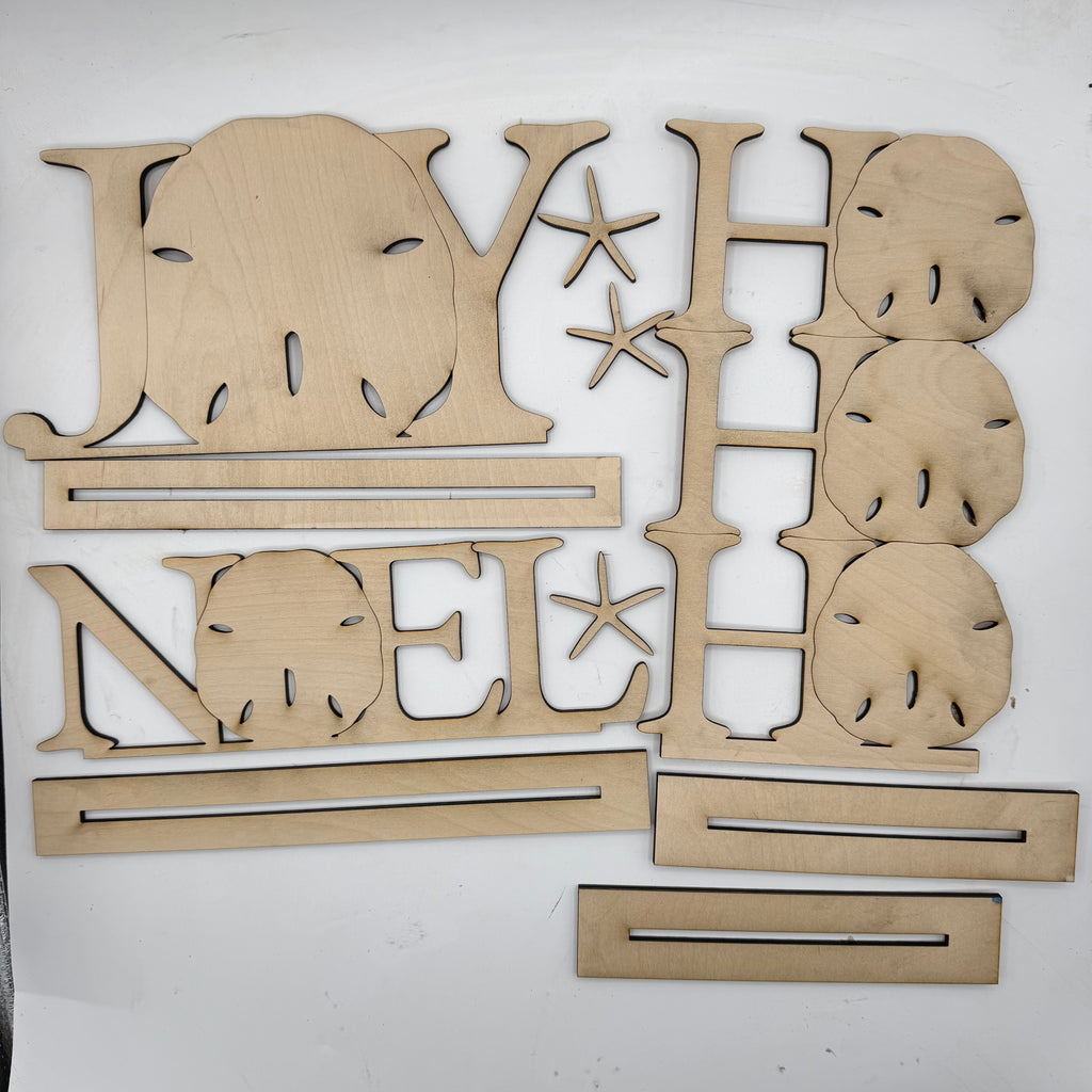 Laser-cut wooden Christmas decorations spelling out 'JOY NOEL HAP' with star accents and shell motifs, arranged on a white background.