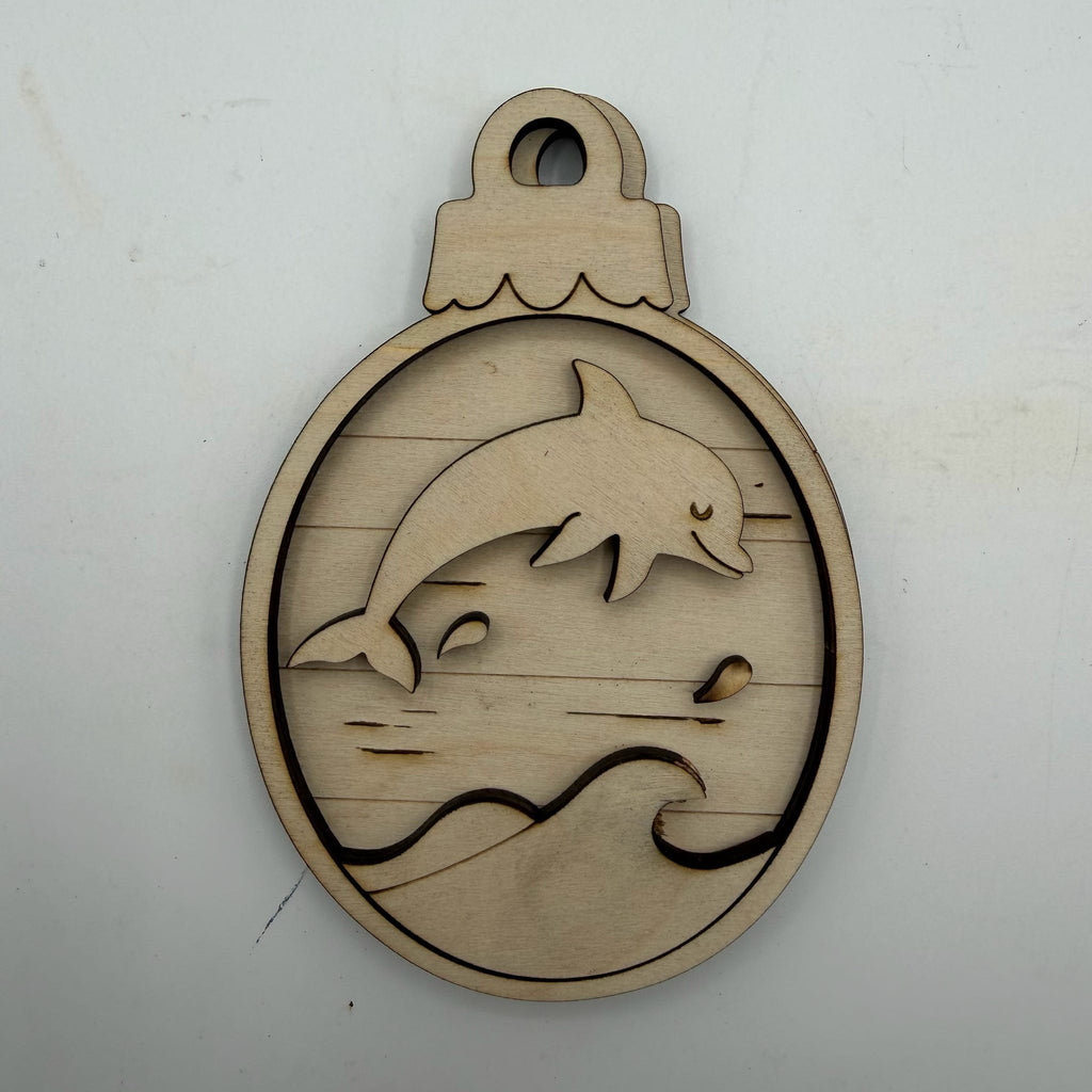 A laser-cut wooden ornament or plaque featuring a dolphin jumping over stylized waves, shown on a plain off-white background.