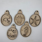 Five oval unfinished wood ornaments with sea-themed engravings, including a dolphin, turtle, starfish, whale, and seahorse, displayed on a light gray background.