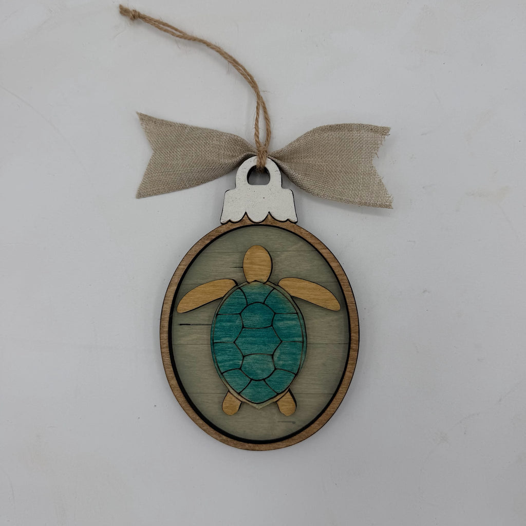 A wooden sea turtle ornament with a teal painted shell and natural wood limbs, hanging from a burlap ribbon bow on a light gray background.