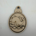 A round laser-cut wooden ornament featuring a whale design, displayed on a light off-white background.