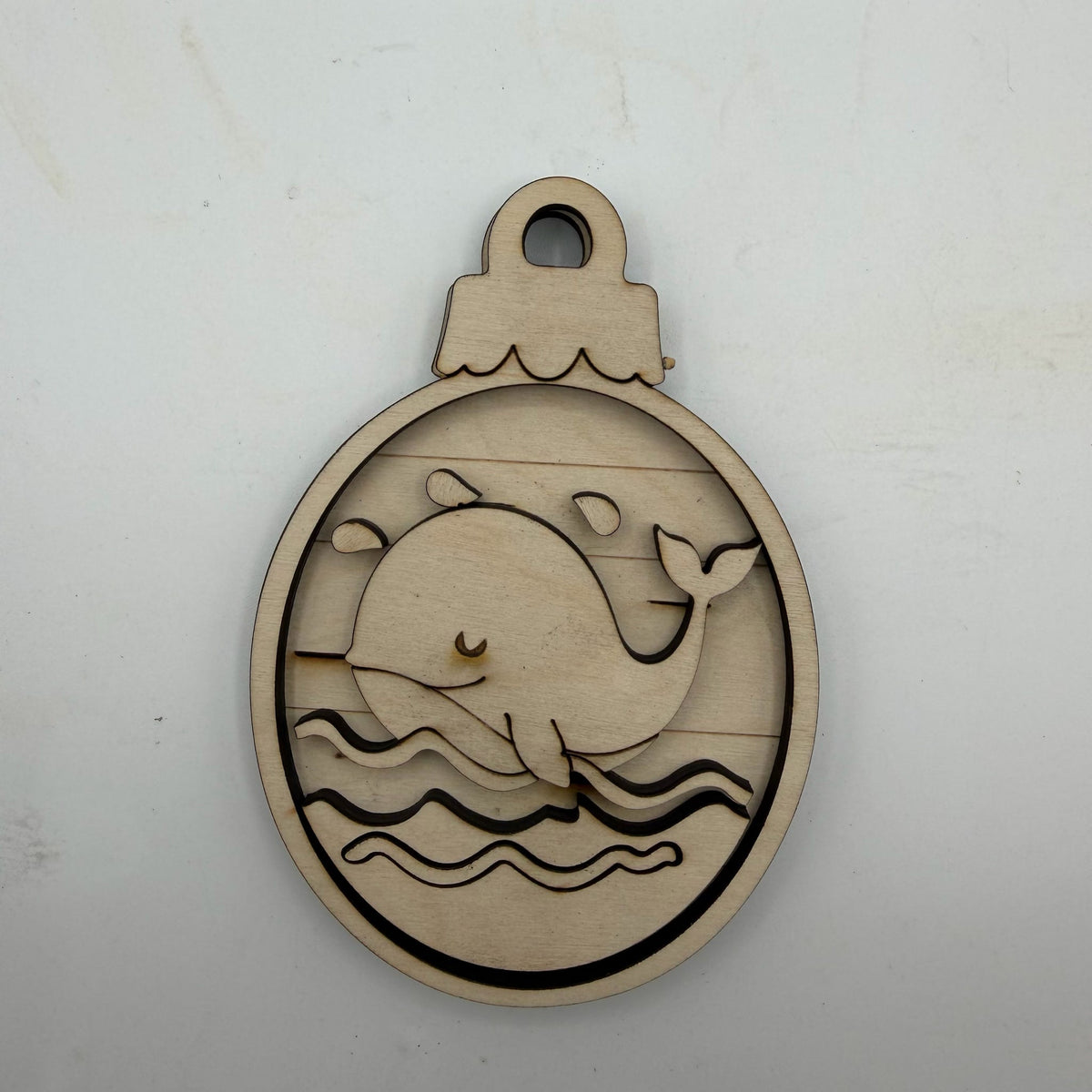 A round laser-cut wooden ornament featuring a whale design, displayed on a light off-white background.