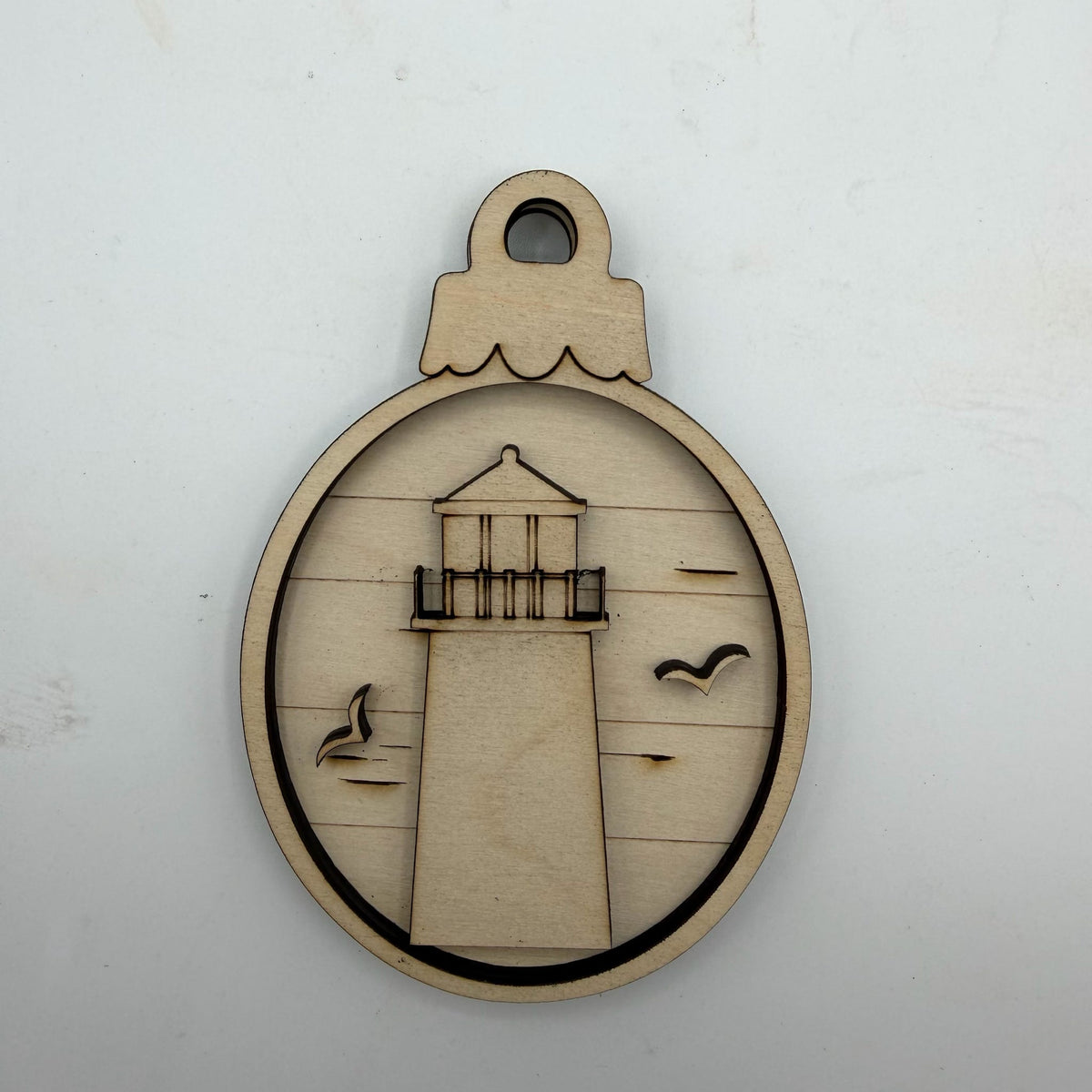 A circular laser-cut wooden ornament featuring a lighthouse design with cutout birds, displayed on a plain white background.