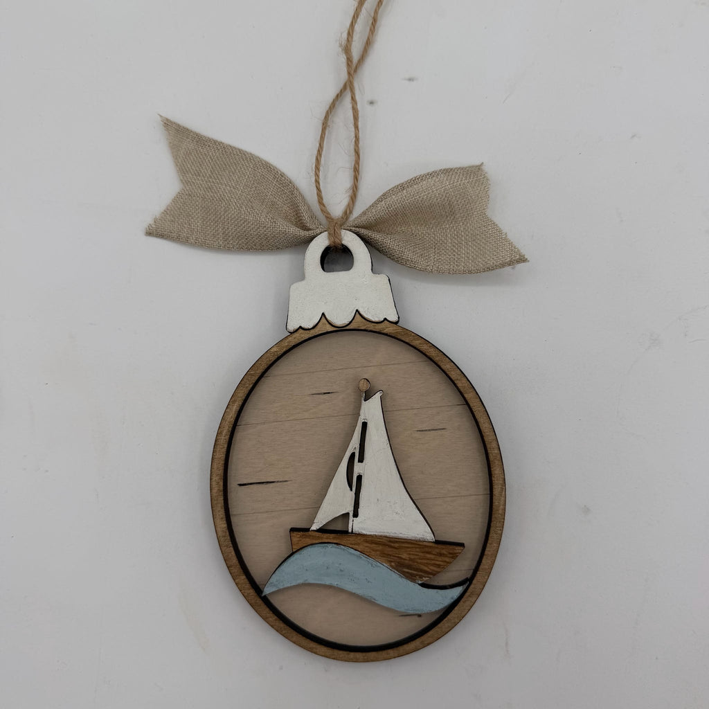 A wooden oval hanging ornament featuring a sailboat design with a light wood sail, brown hull, and light blue wave, suspended from a beige burlap ribbon on a white background.