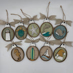 A set of nine oval wooden hanging ornaments with burlap ribbon bows, each featuring a different nautical or beach-themed laser-cut design including a lighthouse, turtle, starfish, dolphin, whale, seahorse, surfboard, sailboat, and Santa Claus.