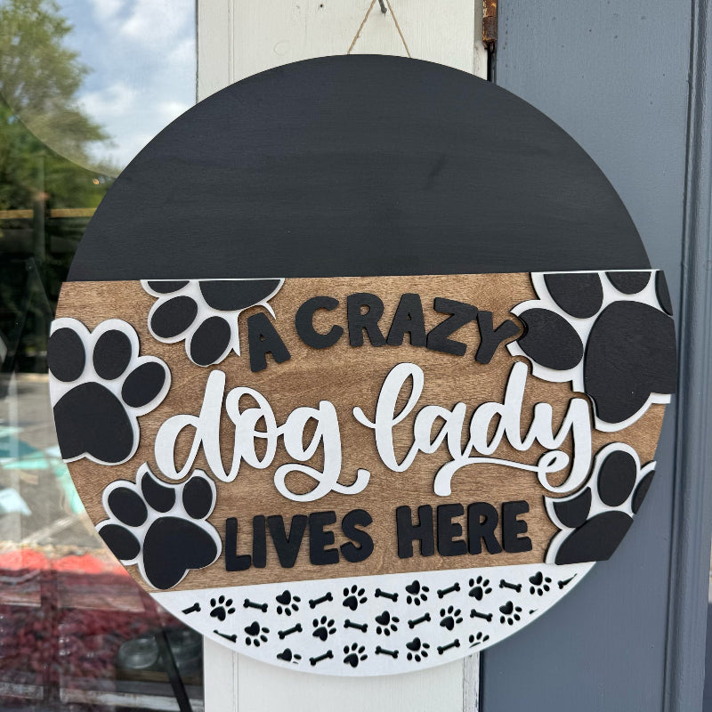 Decorative sign with 'A crazy dog lady lives here' text and paw prints on a door.