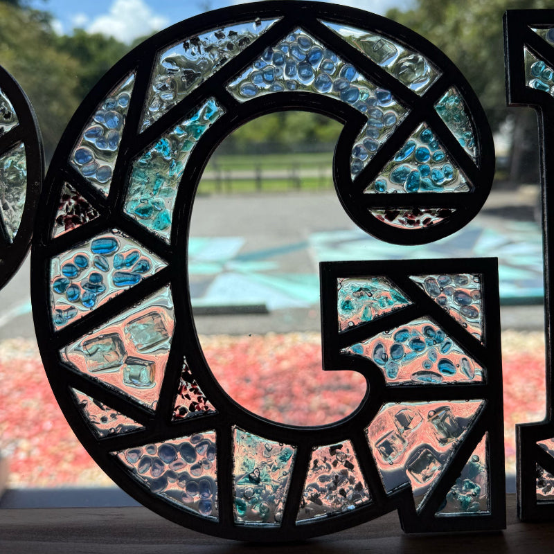Decorative glass panel with blue and pink pebbles in a circular pattern, outdoors.