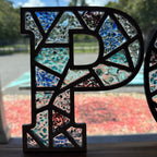 Mosaic letter 'P' with colorful glass pieces on a wooden surface
