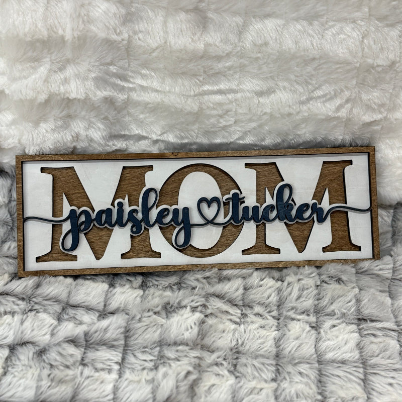Wooden sign with 'MOM' and personalized name on a textured gray background