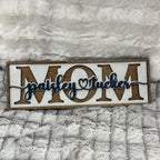 Wooden sign with 'MOM' and personalized name on a textured gray background