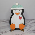 A stuffed toy penguin with a blue and white hat standing on a base, against a white background.