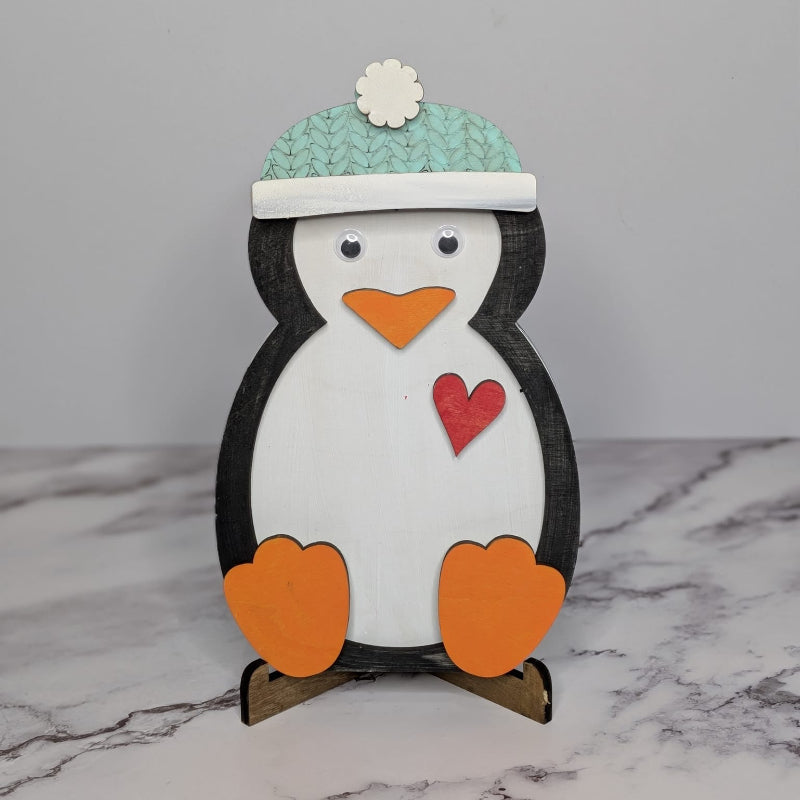 A stuffed toy penguin with a blue and white hat standing on a base, against a white background.
