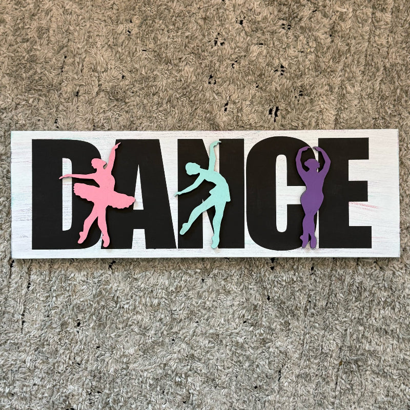 Decorative sign with 'DANCE' and colorful dancer silhouettes on a textured surface