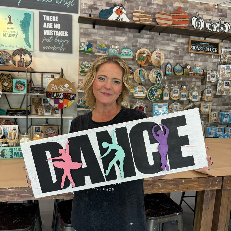 Woman holding a 'DANCE' sign with silhouettes in a store setting