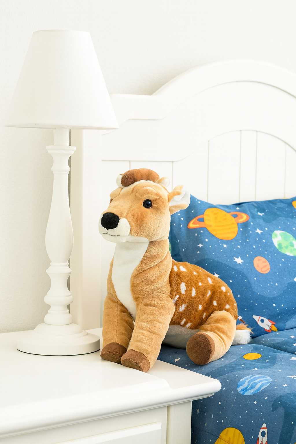 Plush deer toy on a nightstand next to a child's bed with space-themed bedding