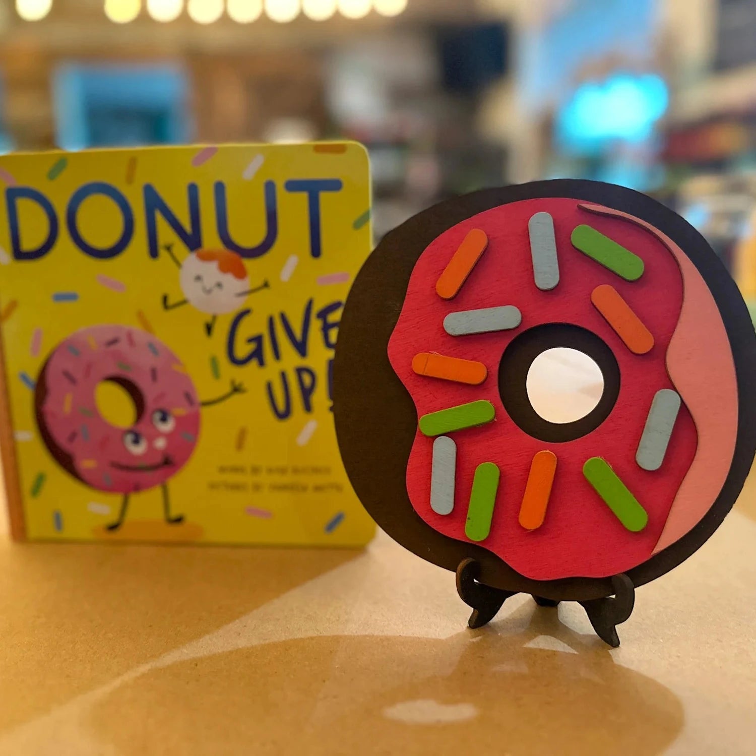 Colorful donut-shaped object on a stand with a book titled 'Donut Give Up' in the background.