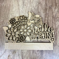 Wooden decorative sign with flowers and butterflies spelling 'hello SPRING' on a wooden background