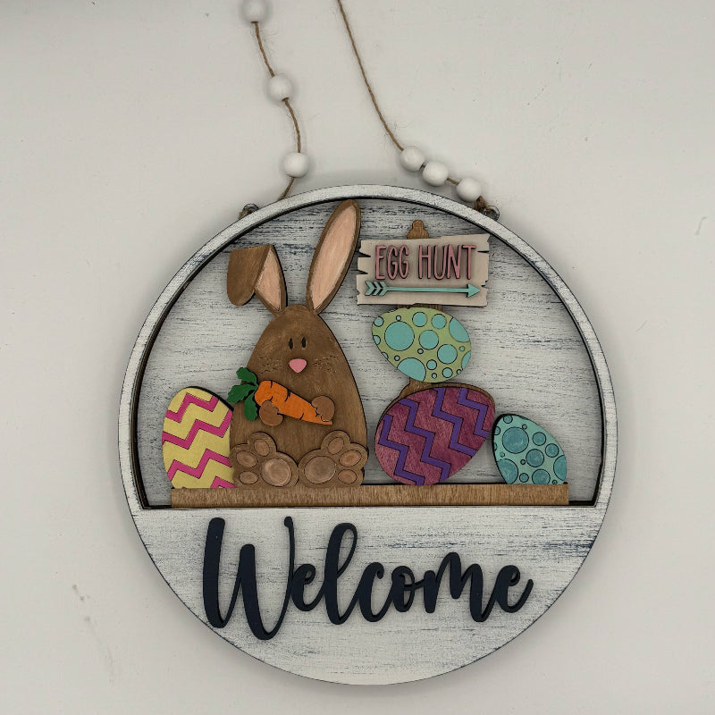 Decorative sign with a bunny and Easter eggs on a wooden hoop, featuring the word 'Welcome'.