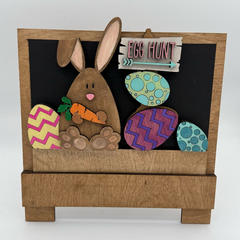 Easter-themed decorative sign with a rabbit, eggs, and 'Egg Hunt' text on a wooden stand.