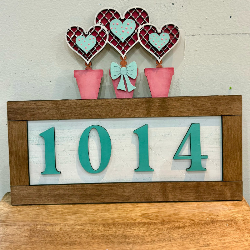 Decorative sign with heart-shaped plants and the number 1014 on a wooden surface.