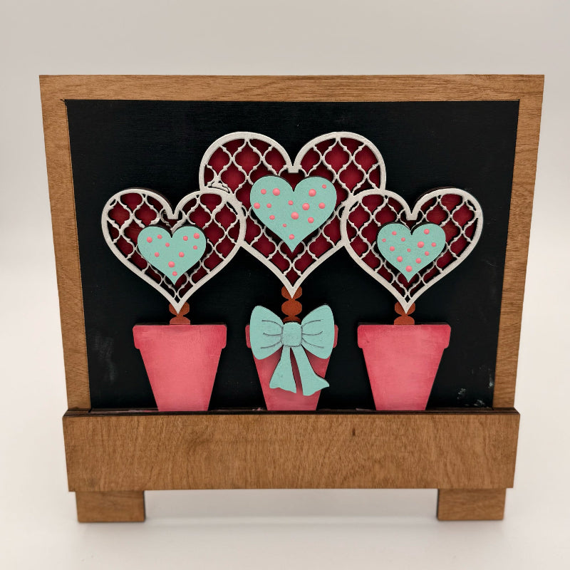 Decorative wall art with heart-shaped plants and a bow on a black background