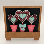 Decorative wall art with heart-shaped plants and a bow on a black background