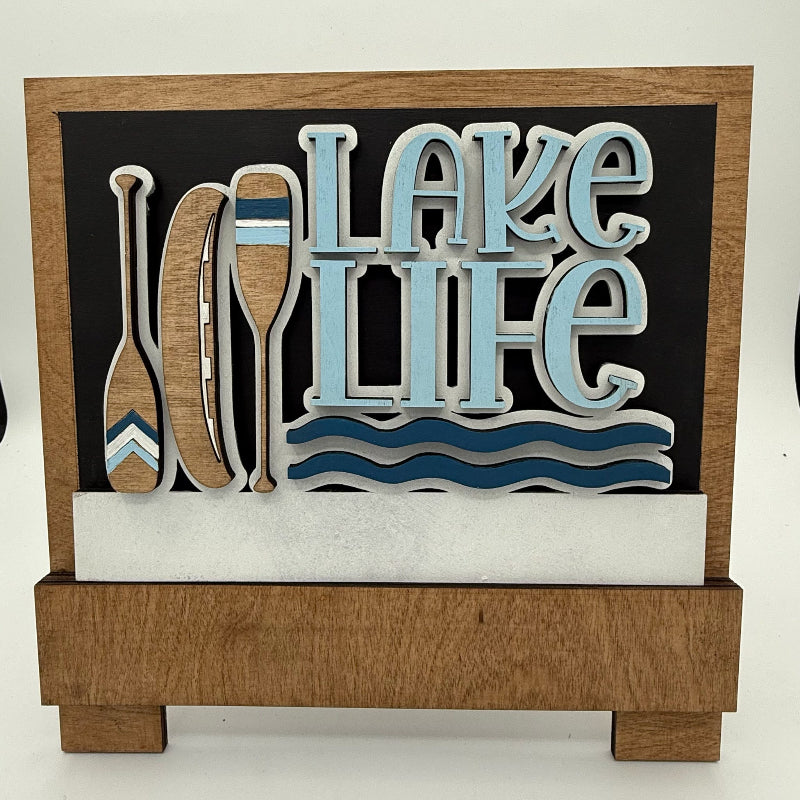 Decorative sign with 'Lake Life' text and oar designs on a black background.