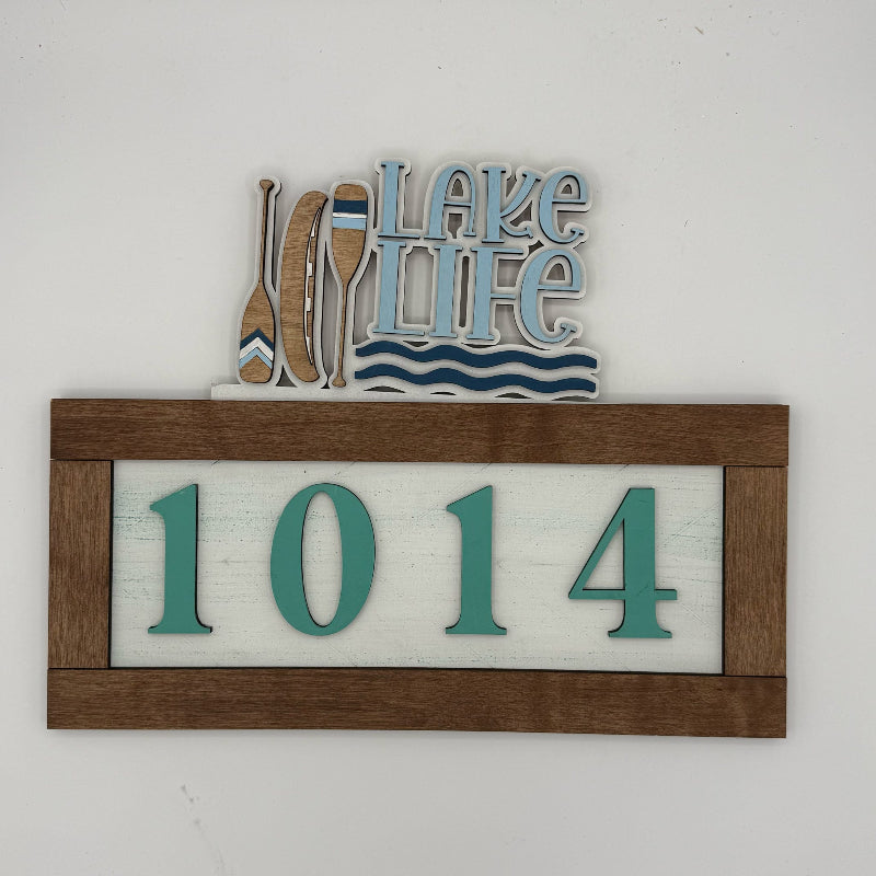 Decorative sign with 'Lake Life' and house numbers '1014' on a white background