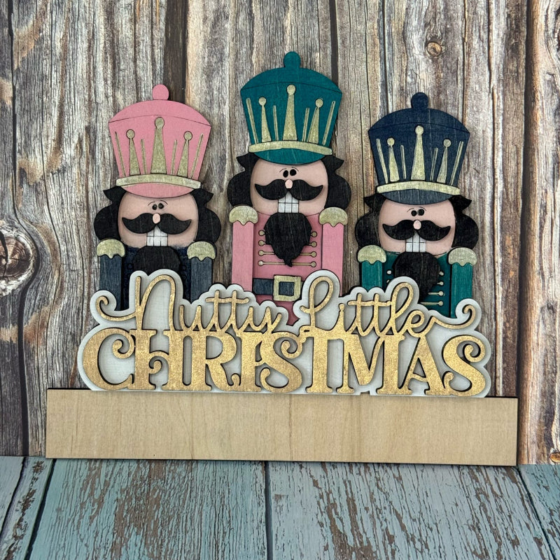 Decorative sign with nutcrackers and 'Nuttie Little Christmas' text on a wooden background
