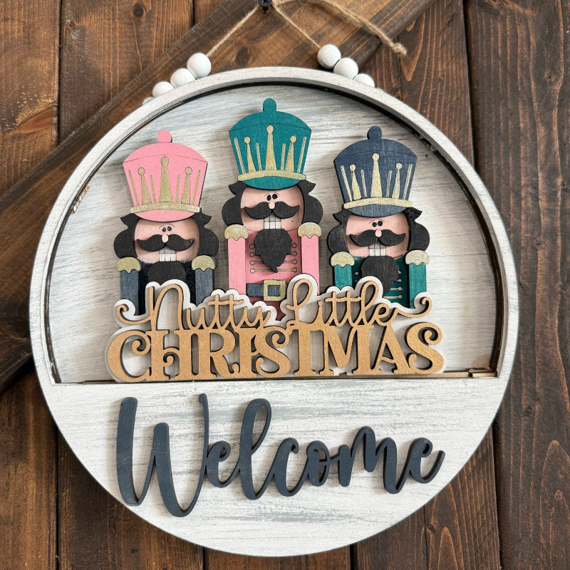 Round wooden sign with Nutcracker design and 'Merry Little Christmas Welcome' text on a wooden background.
