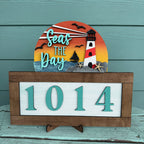 Decorative sign with lighthouse design and text 'Seas the Day' on a wooden stand.