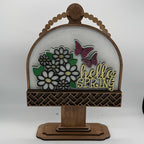 Decorative sign with flowers, butterflies, and 'hello spring' text on a wooden stand.