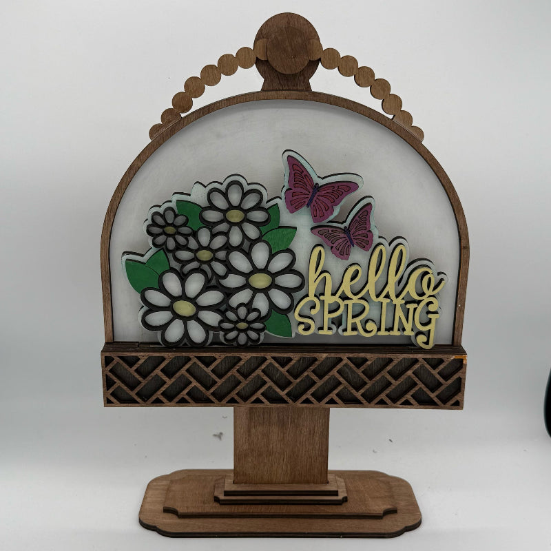 Decorative sign with flowers, butterflies, and 'hello spring' text on a wooden stand.