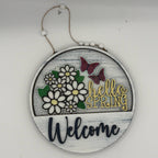 Decorative sign with flowers, butterflies, and 'hello spring welcome' text on a white background