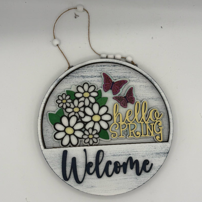 Decorative sign with flowers, butterflies, and 'hello spring welcome' text on a white background