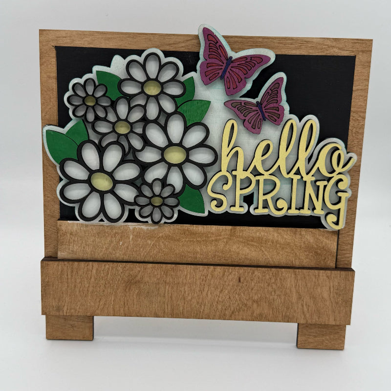 Decorative sign with flowers, butterflies, and 'hello SPRING' text on a wooden base.
