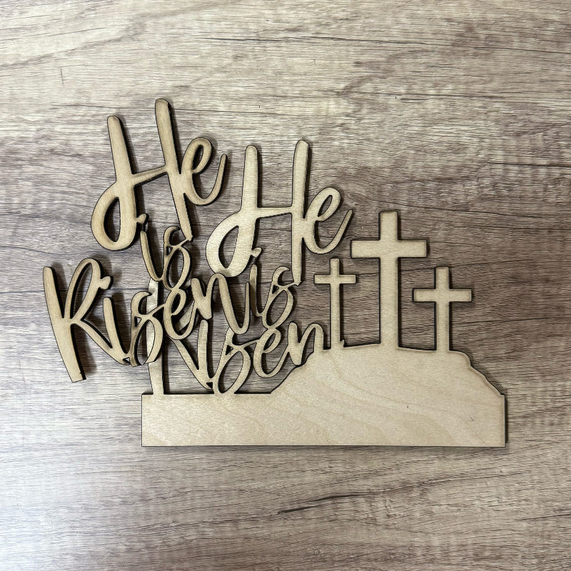 Wooden decorative sign with 'He is Risen' text and crosses on a wooden background