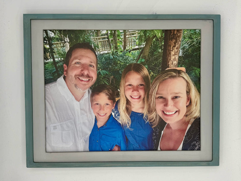 Framed family photo with four smiling people against a natural background