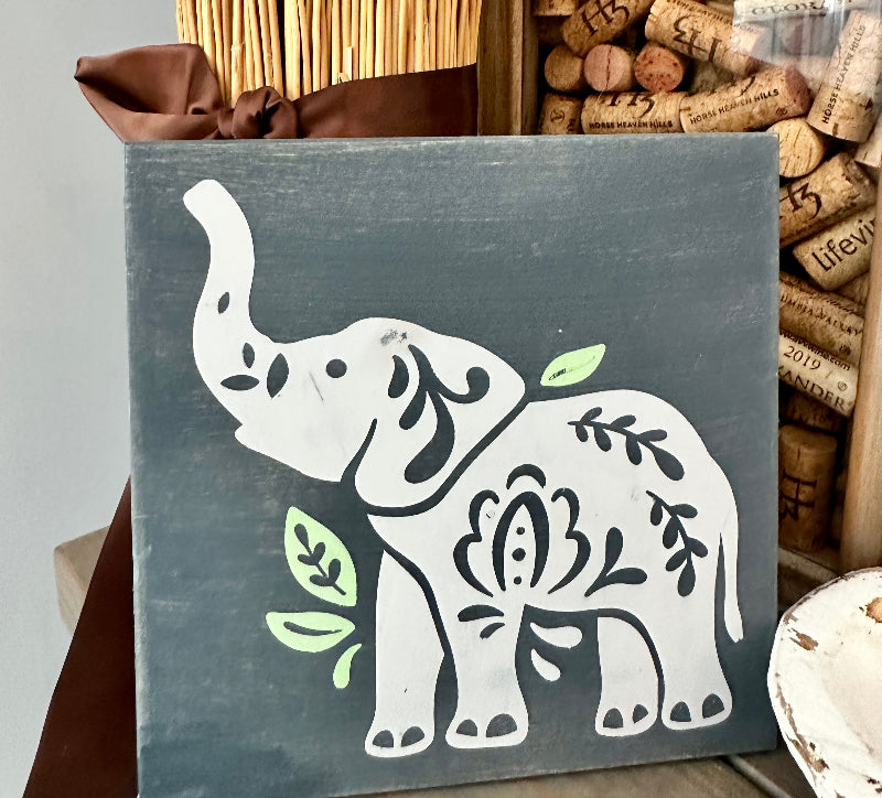 Decorative sign with an elephant design on a gray background, surrounded by wine corks.
