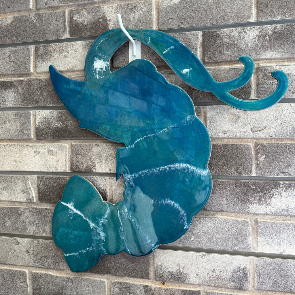 A glossy teal blue abstract wave-shaped wall art piece hanging against a gray brick wall.