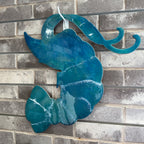 A glossy teal blue abstract wave-shaped wall art piece hanging against a gray brick wall.