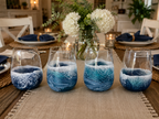 Four blue and white marbled glass tumblers on a dining table with a floral centerpiece.