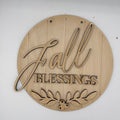 A round, laser-cut wooden sign with the words 'Fall Blessings' and a leafy berry design at the bottom, shown on a plain white background.