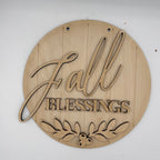 A round, laser-cut wooden sign with the words 'Fall Blessings' and a leafy berry design at the bottom, shown on a plain white background.