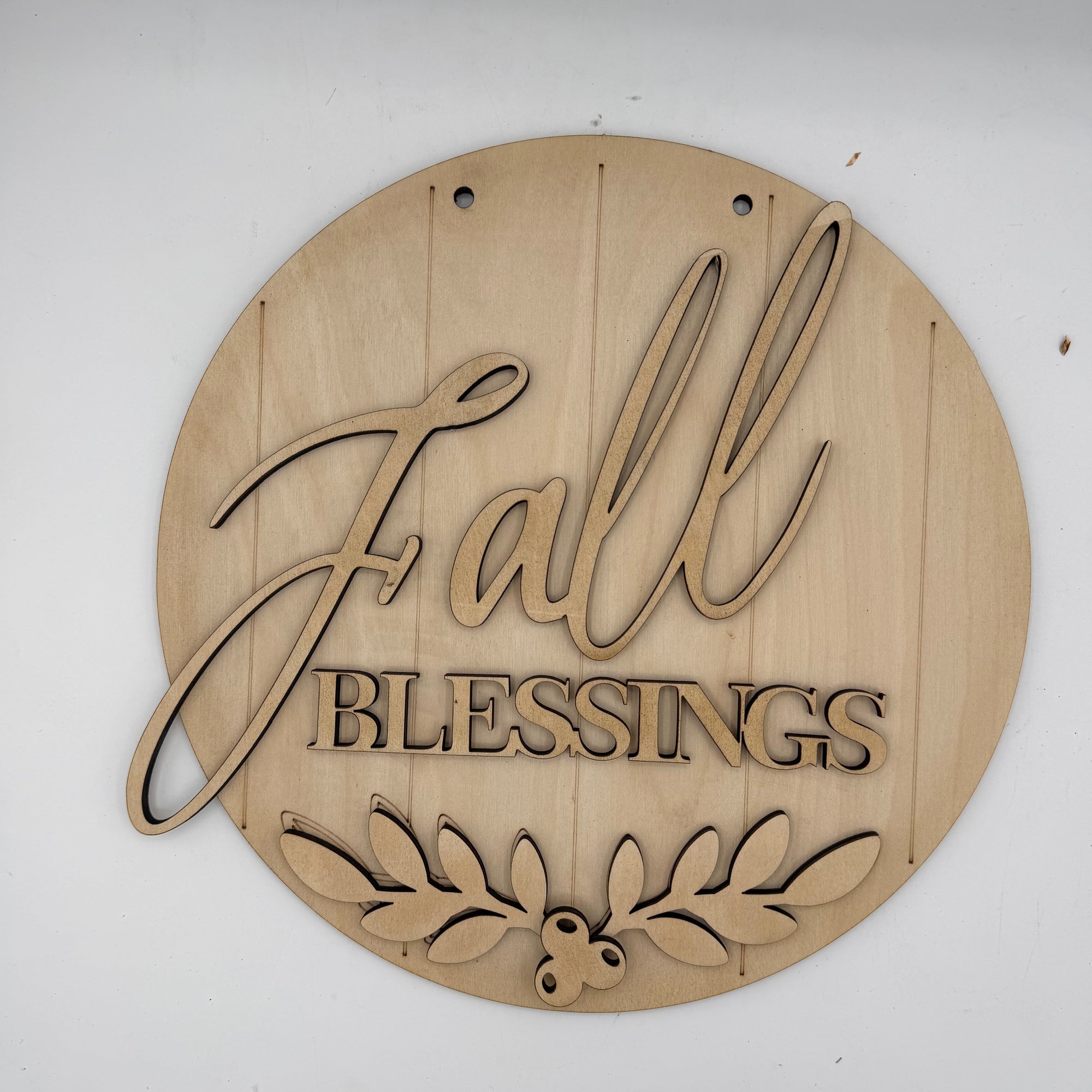 A round, laser-cut wooden sign with the words 'Fall Blessings' and a leafy berry design at the bottom, shown on a plain white background.