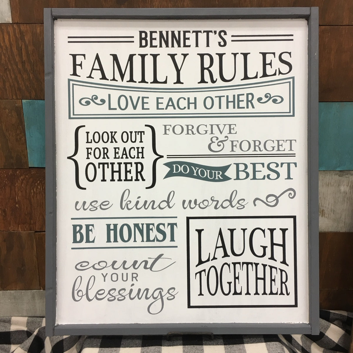 A personalized family rules sign with various phrases written in different fonts and colors, framed in a gray wood frame.