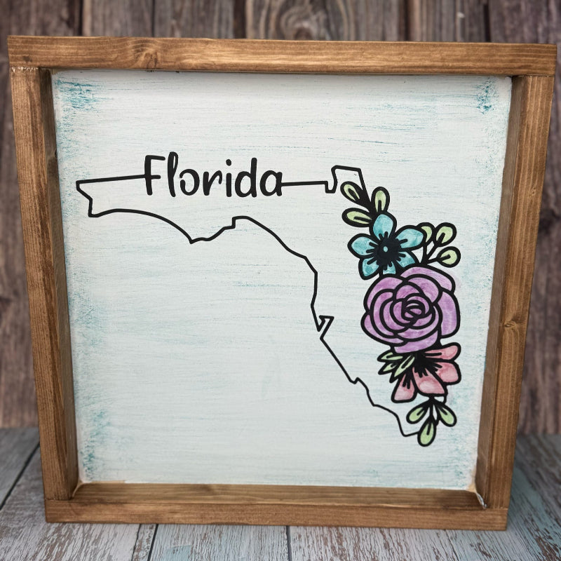 Framed artwork of Florida with floral design on a wooden surface