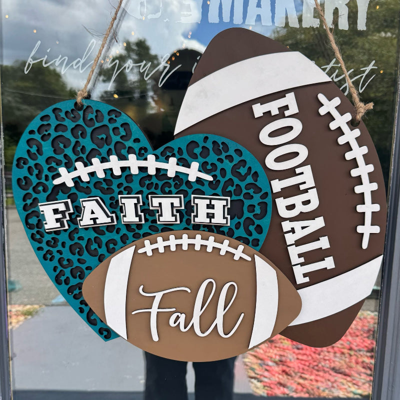 Decorative sign with football and heart shapes with text 'Faith', 'Football', and 'Fall' on a glass door.