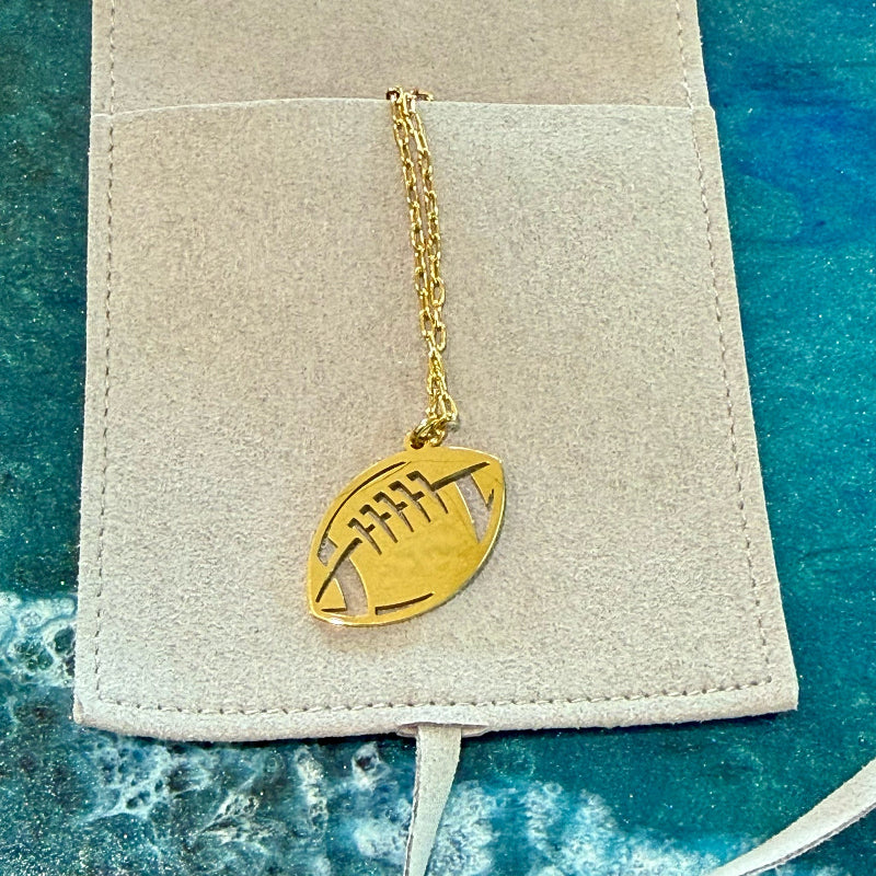Gold football-shaped pendant on a chain against a textured beige background